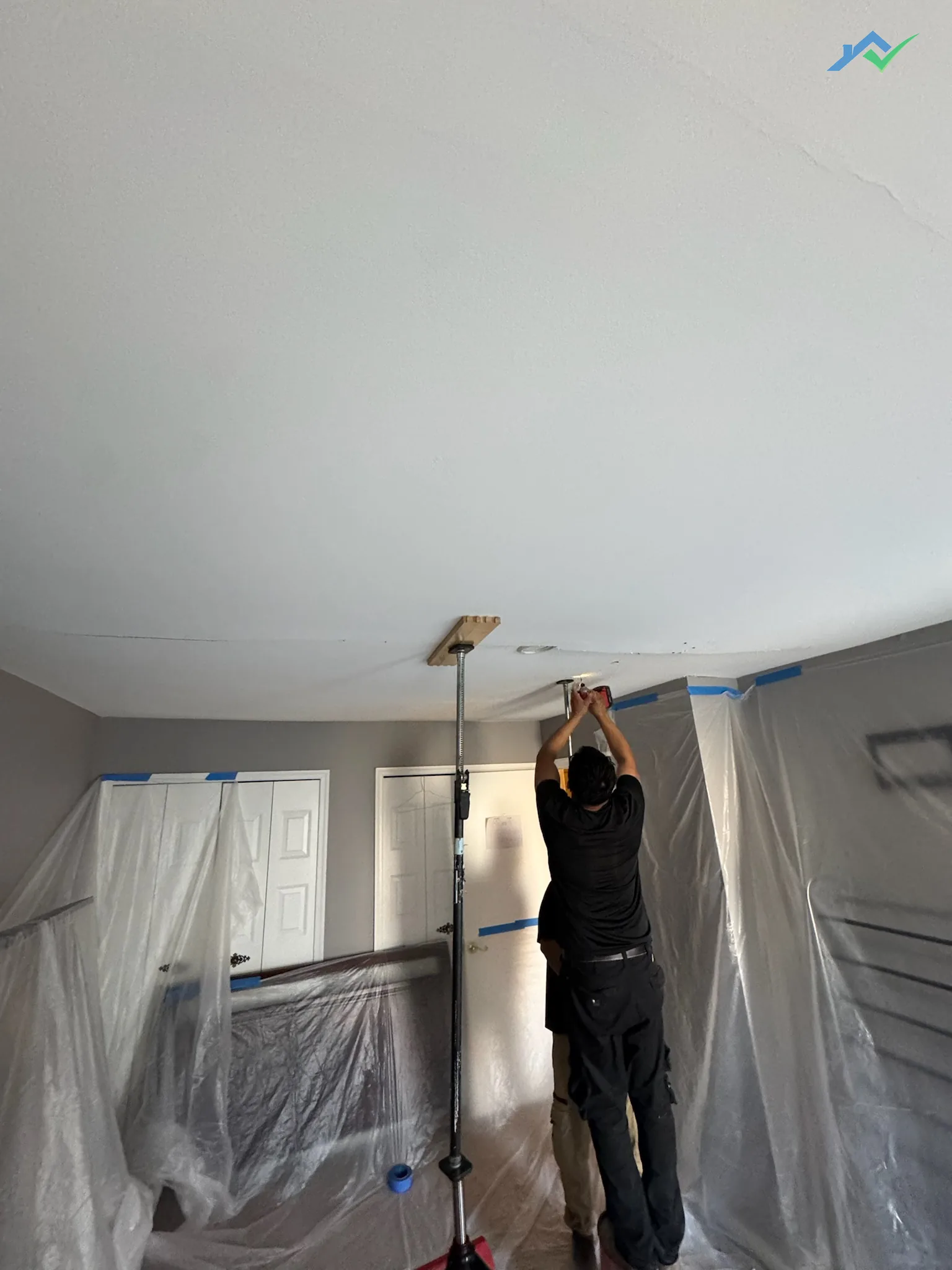 A ceiling jack braced under the sagging Burke ceiling while a crew member drives screws overhead on the first repair attempt.