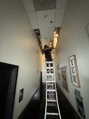 HouseWorks tech replacing drop ceiling tiles on tall ladder in Ashburn VA restaurant hallway