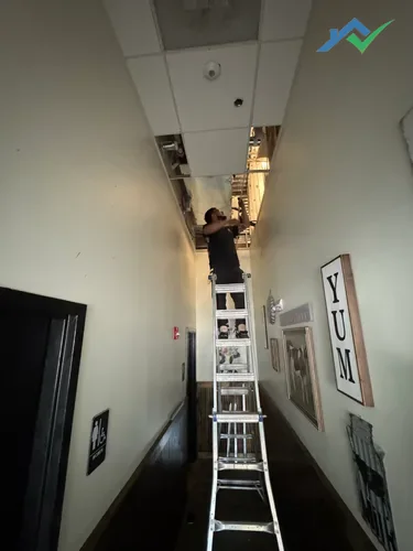 HouseWorks tech replacing drop ceiling tiles on tall ladder in Ashburn VA restaurant hallway