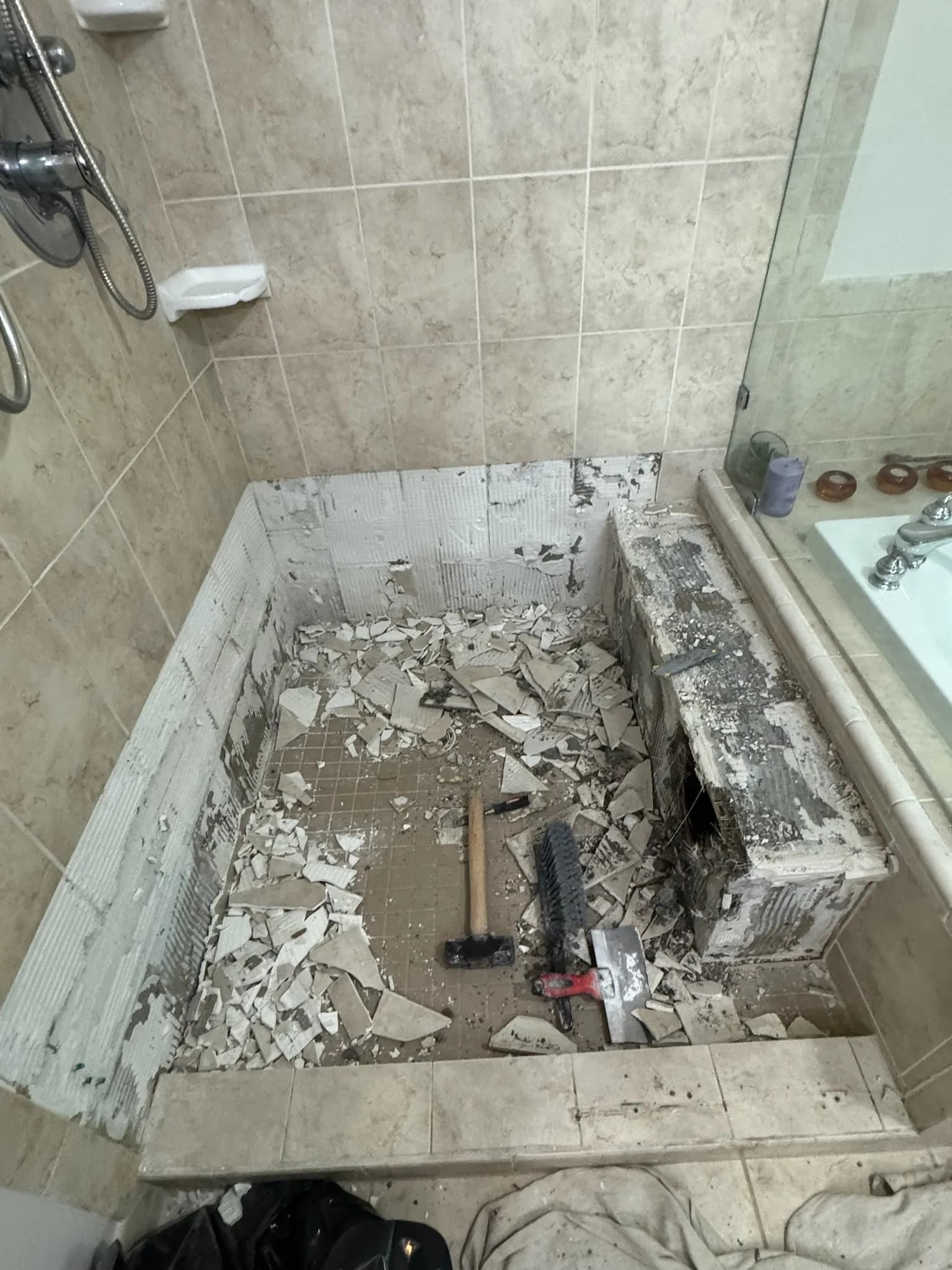 Shower pan demolition underway — the old mortar bed and tile stripped to the substrate.