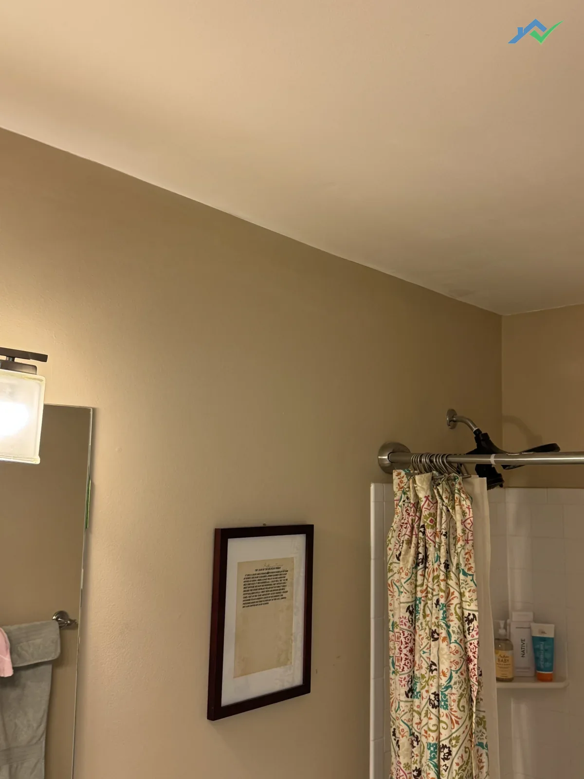 Same Purcellville, VA bathroom ceiling after repair — the brown water stain is gone, the ceiling above the shower and framed picture is now uniformly clean with stain-blocking primer sealed in and repainted so nothing bleeds back through.
