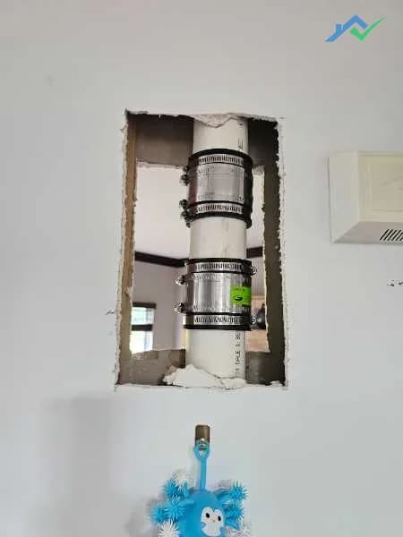 Before shot from the Purcellville, VA homeowner — a large rectangular access hole cut into the drywall exposing a stack pipe with couplings, left rough after plumbing work and waiting to be re-blocked and patched.