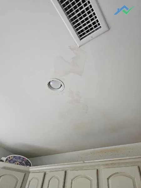 Before shot of the kitchen ceiling in this Purcellville, VA home — a brown tannin water stain trailing around the louvered HVAC supply vent and past the recessed light, right above the cream-colored kitchen cabinets, from a leak that had since been resolved but never sealed or repainted.