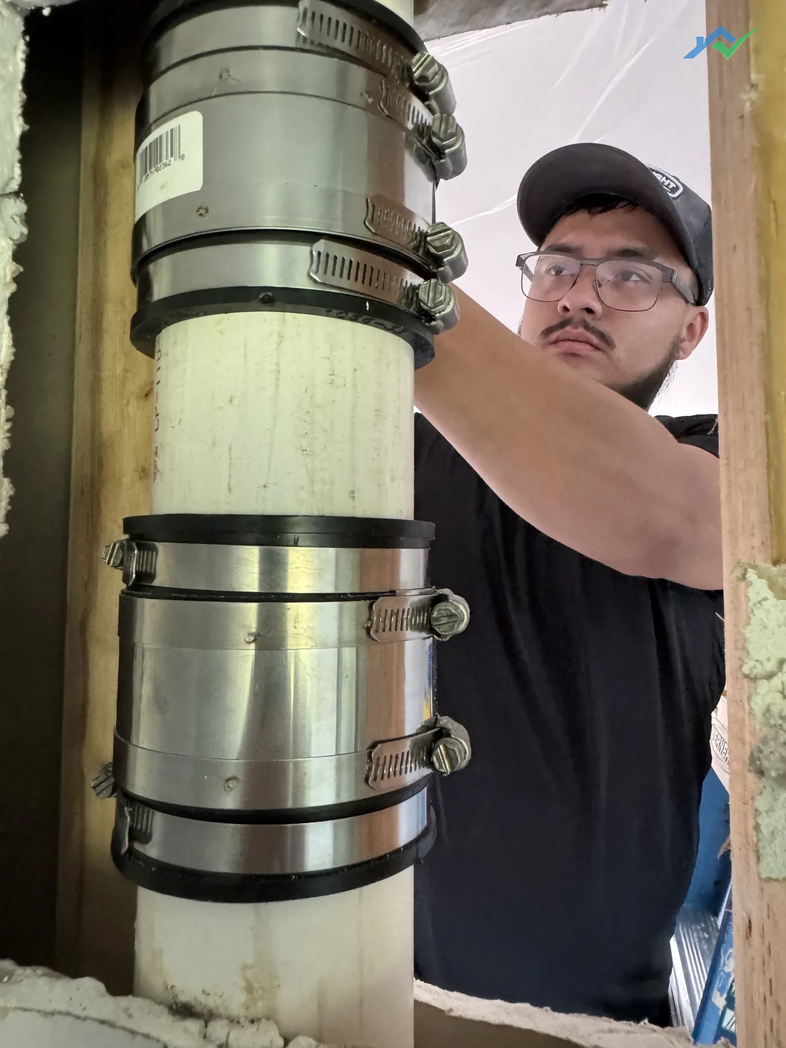 HouseWorks tech Eduardo reaching into the opened wall cavity in this Purcellville, VA home, checking the plumbing stack and couplings before setting blocking so the drywall patch has something solid to fasten to.