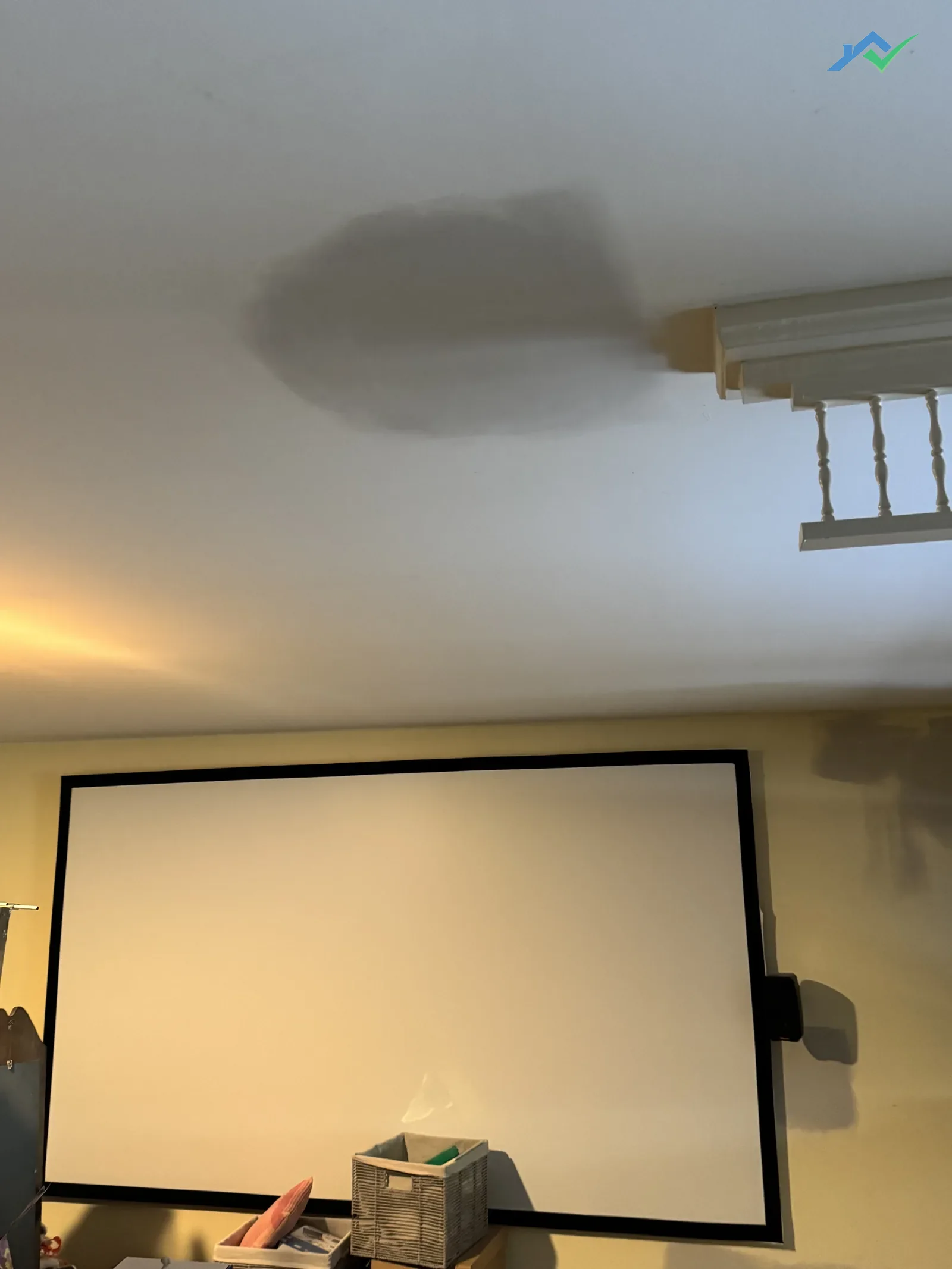 Mid-repair ceiling patches in the Purcellville, VA home with fresh joint compound feathered out around each patched section, drop cloth on the floor and the TV wrapped in plastic while the mud cures.
