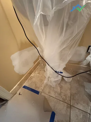 Floor and bathroom fixtures protected with plastic sheeting and tape prior to drywall patching.
