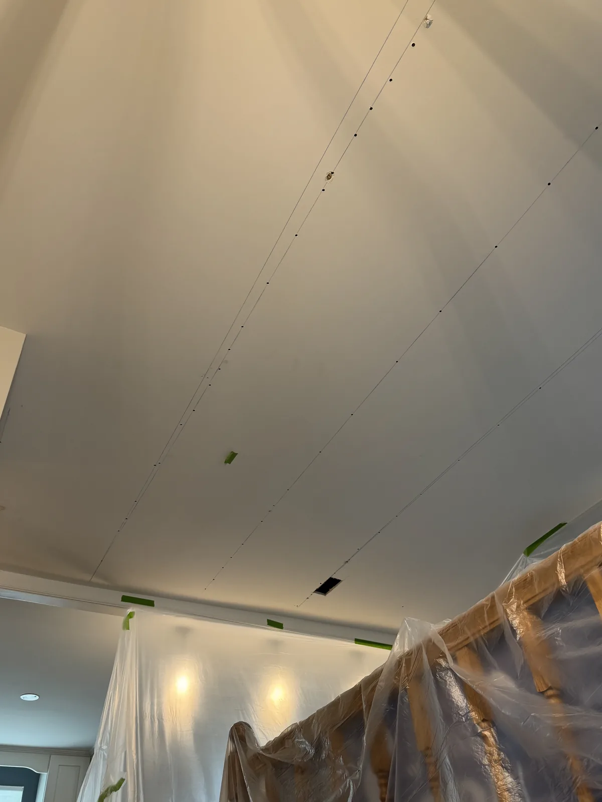 Chalk lines snapped across the ceiling in this Herndon, VA home marking the joist locations — this layout guides where new fasteners go to re-secure the drywall panels above. All the furniture below is wrapped in plastic containment.